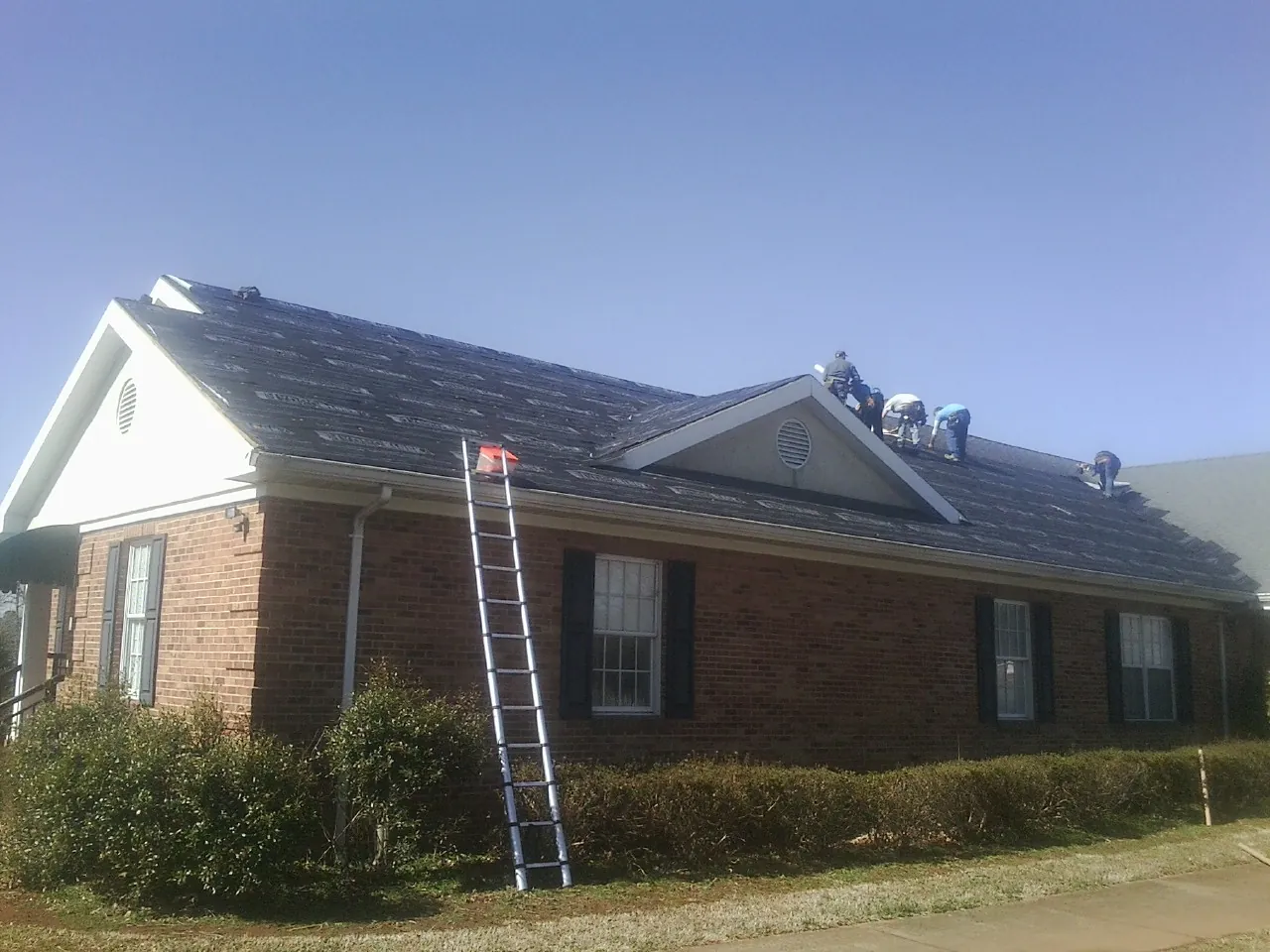 Crew tearing shingles off a brick ranch roof with a ladder set — Emergency Roof Repair work by our crew in Aiken