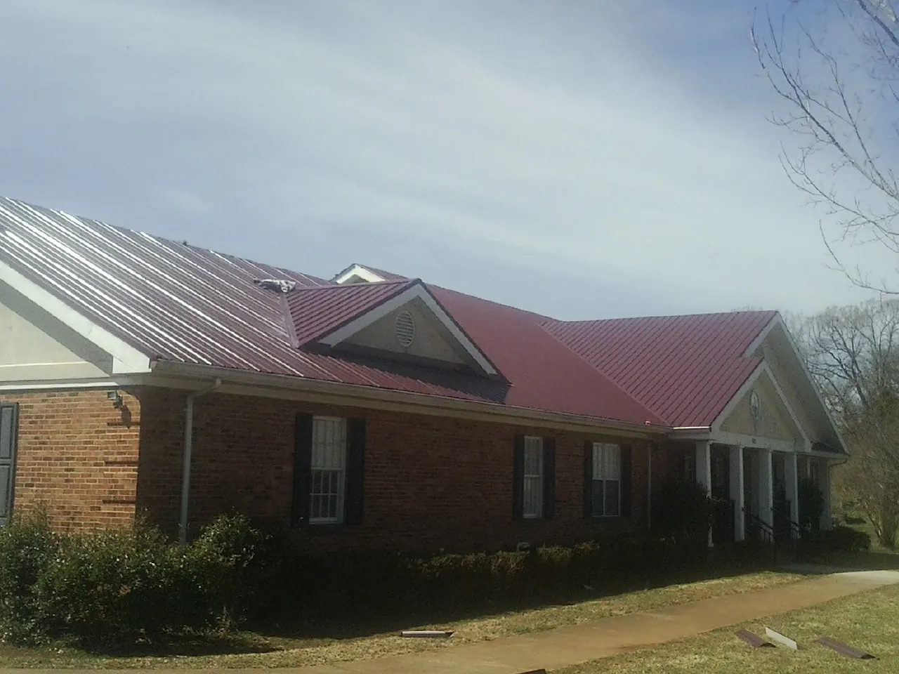 Red metal roof with gabled entries on a long brick building, from a Hail Damage Roof Repair job in Aiken