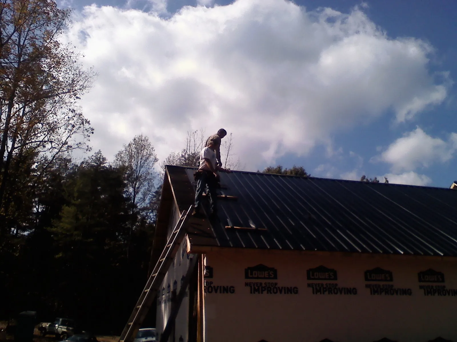 Roofer fastening dark metal panels high against a cloudy sky, from a Roof Inspection job in Aiken